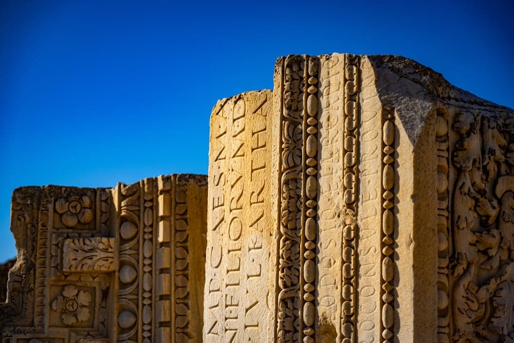 Ancient Roman stone carvings with Latin inscriptions against a bright blue sky in Tunis, Tunisia.
