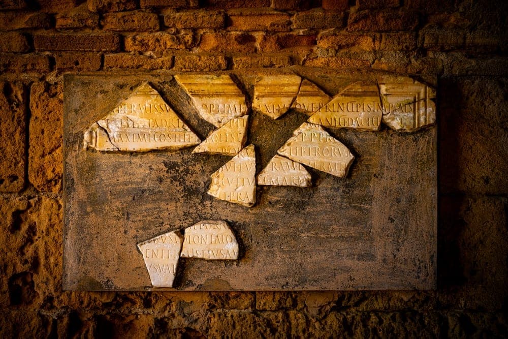 Fragmented ancient Roman inscriptions on stone, displayed on a brick wall in Tunis, Tunisia.