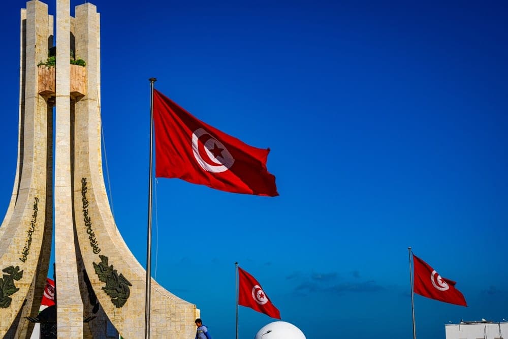 The Monument of the Tunisian Republic in Tunis, Tunisia, with three red Tunisian flags flying against a bright blue sky.