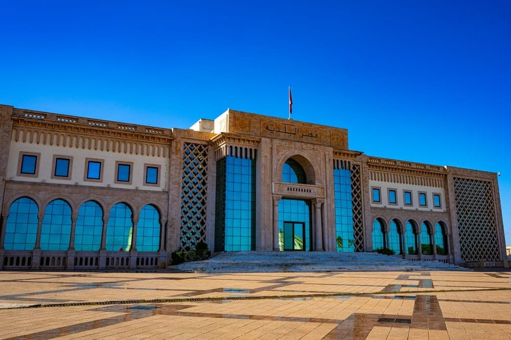 The Municipality of Tunis building, a modern structure with traditional accents, set against a clear blue sky with a paved plaza in the foreground, Tunis, Tunisia.
