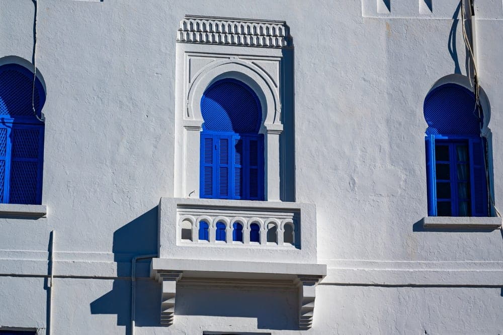 White building with bright blue shutters and arched windows in Tunis, Tunisia.