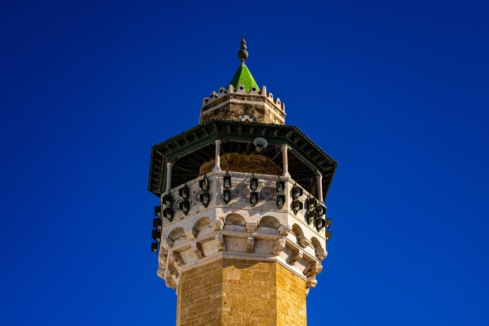 The octagonal sandstone minaret of Djamaa el-Kebir mosque in Tunis, Tunisia, against a clear blue sky.