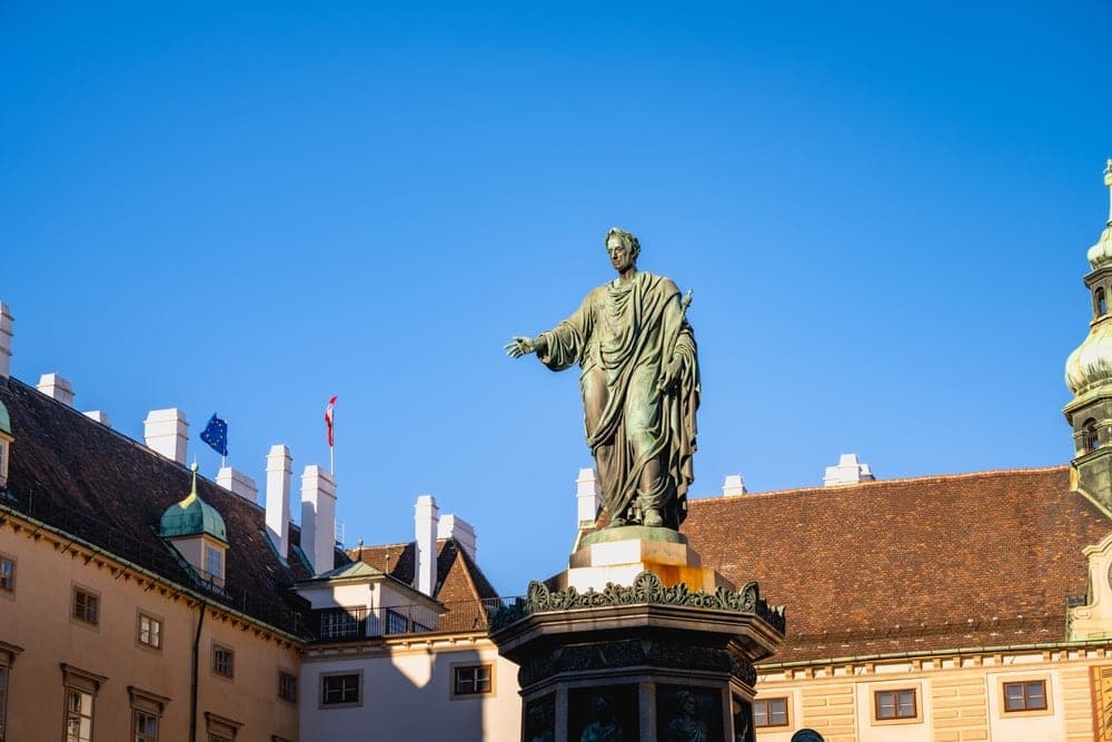 Bronze statue of Emperor Joseph II in front of historic buildings in Vienna, Austria, under a clear blue sky.