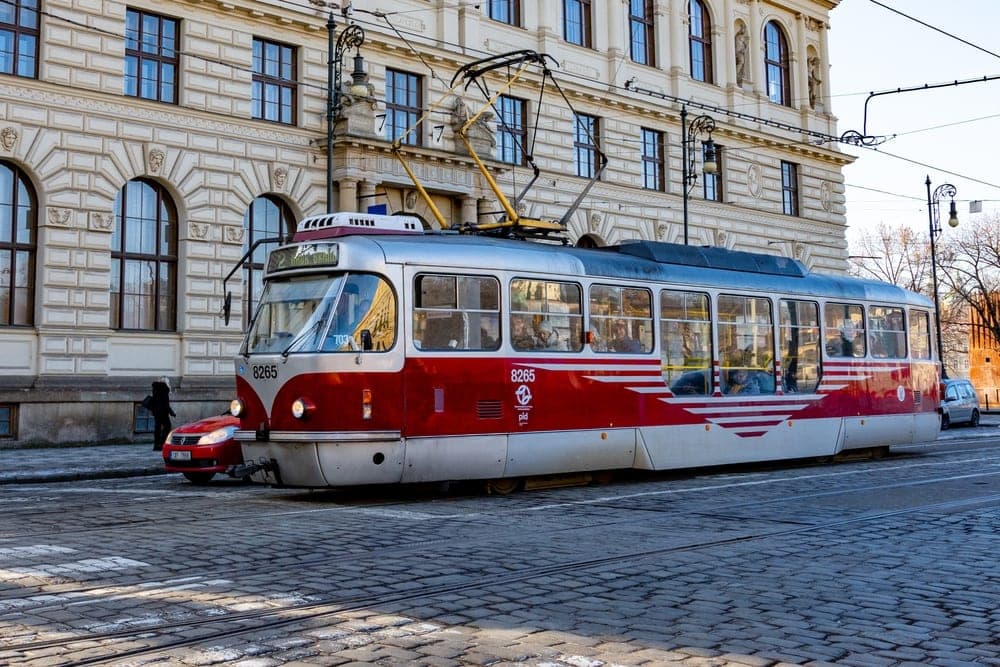 A red and silver tram on a cobblestone street in Prague, Czech Republic, with a historic building in the background.