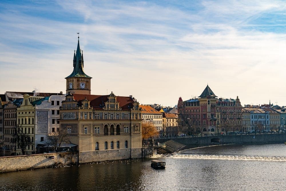View of the Vltava River and historic buildings in Prague, Czech Republic, under a bright sky.