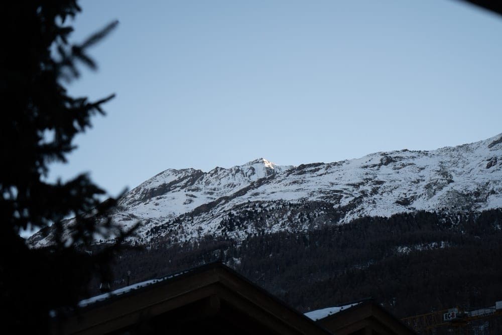 Snow-capped Swiss Alps mountains in Zermatt, Switzerland, illuminated by the first rays of sunlight, with dark coniferous trees in the foreground.