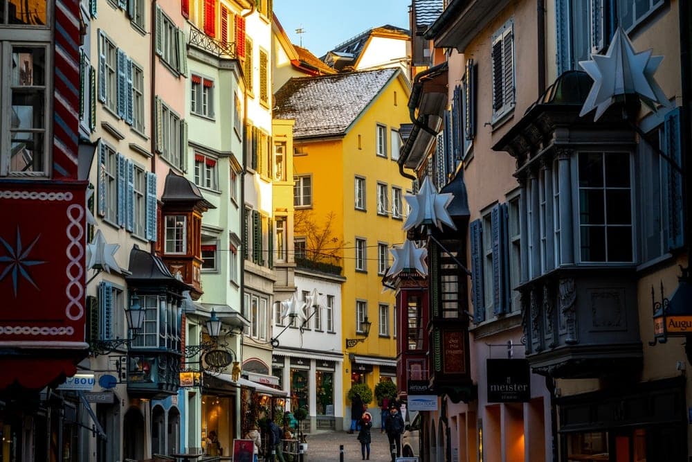 A charming street in Zürich, Switzerland, bathed in the warm glow of late afternoon sun, with colourful buildings lining a cobblestone path.