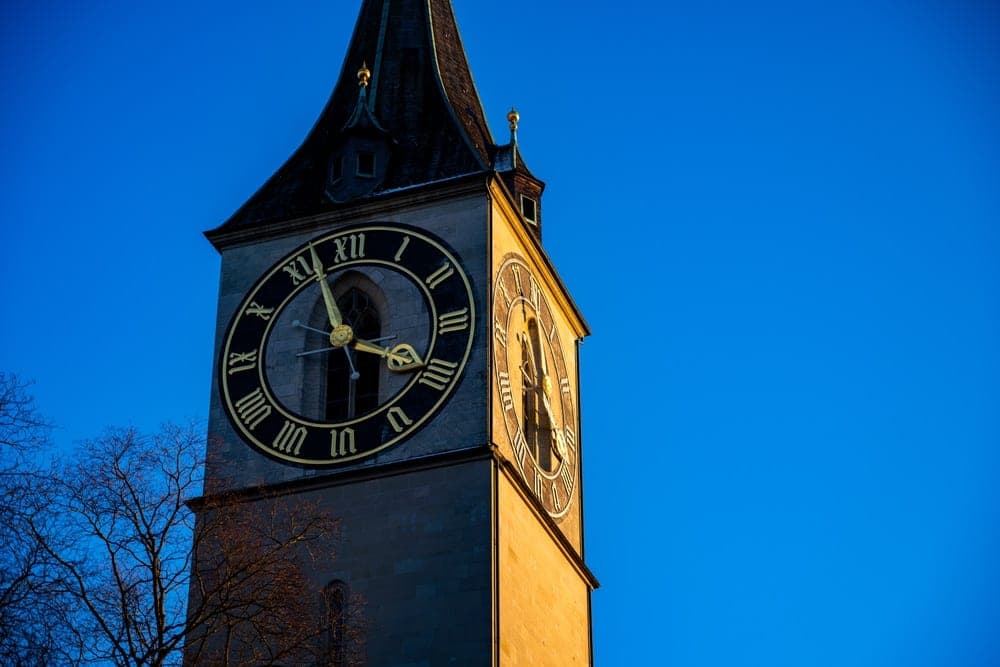 The imposing clock tower of St. Peter's Church in Zürich, Switzerland, bathed in golden late afternoon sunlight against a deep blue sky.