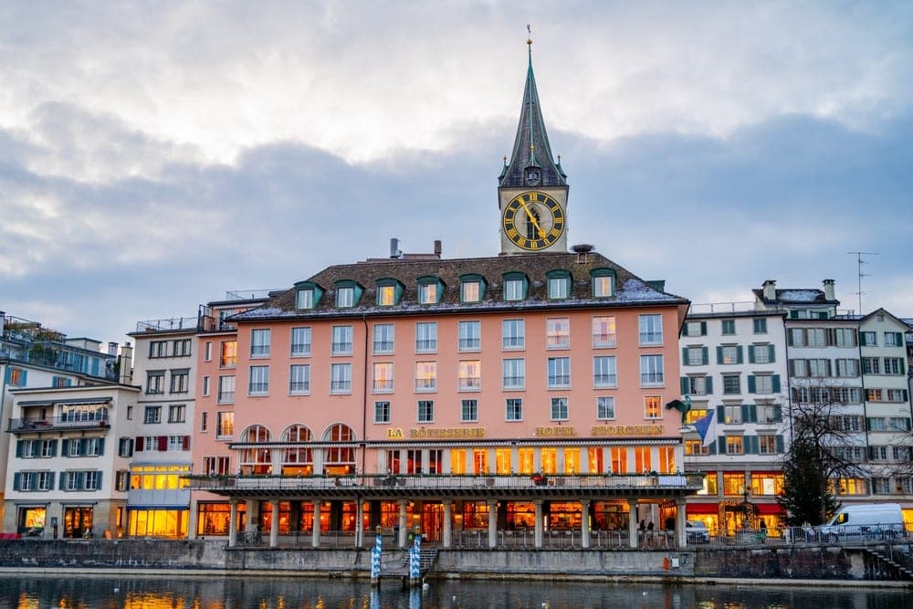 The Hotel Storchen and St. Peter Church clock tower reflected in the Limmat river in Zurich, Switzerland.