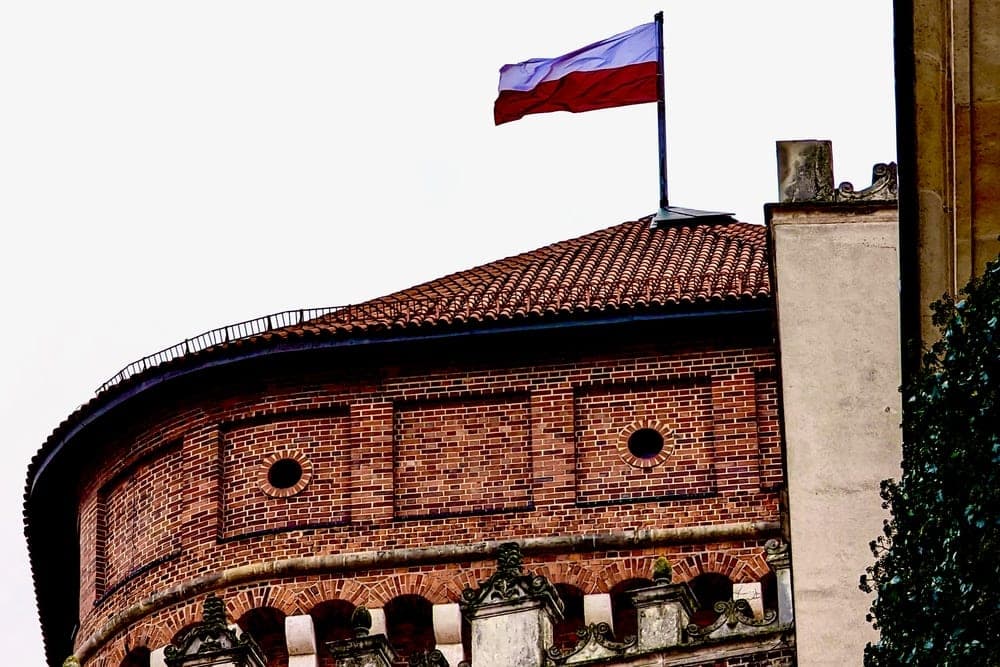 The Polish flag flying atop a historic red-brick tower at Wawel Castle in Krakow, Poland.