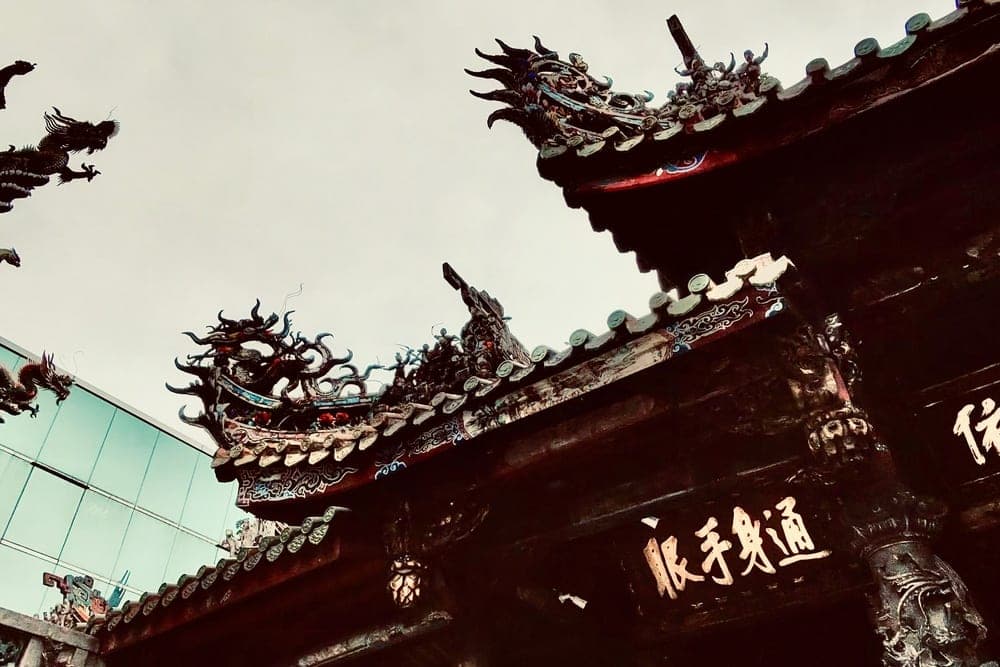 Ornate dragon carvings on a traditional Taiwanese temple roof in Taipei, Taiwan, with a modern glass building in the background.